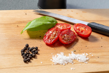 Geschnittene Cherrytomaten mit Basilikumblatt, Salz, Pfeffer und Tomatenmesser auf einem...