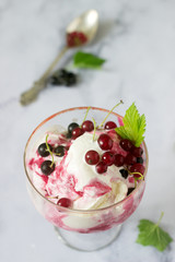 Creamy ice cream with red and black currants in a glass on a light table.