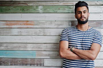 Handsome tall arabian beard man model at stripped shirt posed outdoor against wooden background....