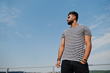 Handsome tall arabian beard man model at stripped shirt posed outdoor against sky. Fashionable arab guy.