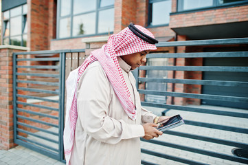 Middle Eastern arab man posed on street against modern building with tablet at hands.