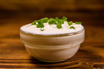 Glass bowl with sour cream and chopped green onion on wooden table