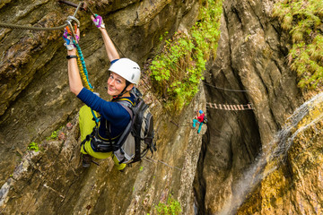 Active young girl on via ferrata in deep canyon creek with waterfall in background, Postalmklamm,...