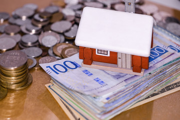Mortgage house loan, real estate tax, macro financial Concept, Scandinavian house model with pile of banknotes and coins money on brown wooden shiny surface table, with copy space.