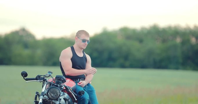 Handsome guy is sitting on a motorcycle and holding a cigarette in his hand. Guy smokes
