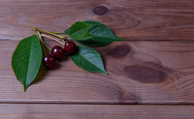 Ripe cherries with leaves on a wooden background.