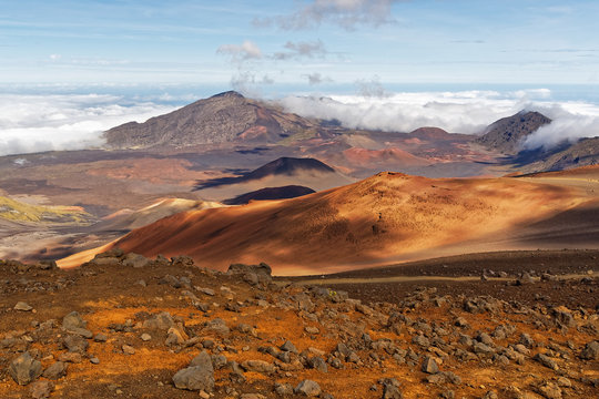 Wide volcanic landscape with lava fields in different colors, wide view, ocher shades, reds, stones in the foreground, cloud shadows, contrast - Location: Hawaii, Island Maui, volcano "Haleakala"