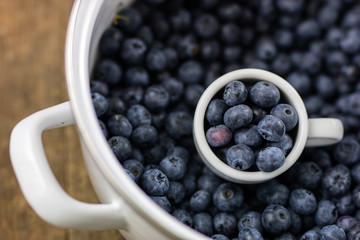 Ripe blueberry fruit in a container on a wooden kitchen table. Fruit prepared for dessert.