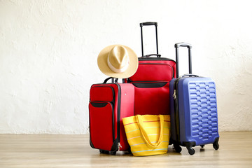 Three suitcases, red textile & blue hard shell luggage, extended telescopic handle, straw hat, yellow beach bag, white textured wall background. Couples retreat trip concept. Close up, copy space