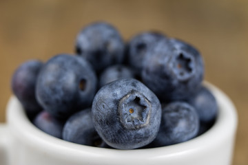 Ripe blueberry fruit in a container on a wooden kitchen table. Fruit prepared for dessert.