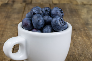 Ripe blueberry fruit in a container on a wooden kitchen table. Fruit prepared for dessert.