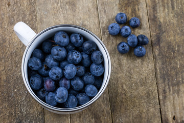 Ripe blueberry fruit in a container on a wooden kitchen table. Fruit prepared for dessert.