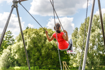 A girl in a red shirt plays on a swing, on a lovely sunny day