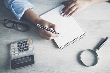 Woman hand notepad with calculator on wooden table background