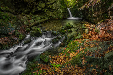 Obraz premium A waterfall hidden in rocks. Amazing nature scene. Landscape. Flowing water. Stones, trees, water.