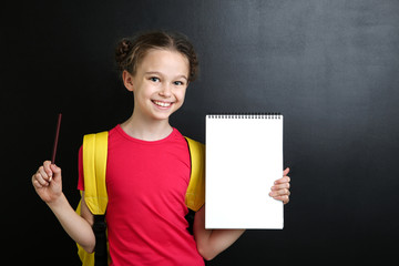 Young girl with notebook and pencil on blackboard background