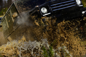 Competition, energy and motorsport concept. Car racing with dirty road. Off road vehicle or SUV crossing puddle with dirty water and mud splash, close up