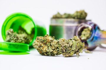 Marijuana buds up close in foreground with blown glass pipe and grinder against white background