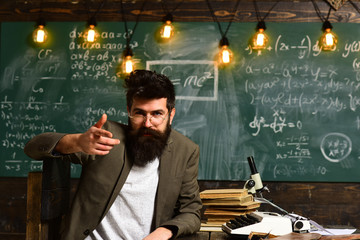 Confident teacher sit at desk. Businessman with beard in suit. Bearded man with typewriter, books and microscope. Scientist in eyeglasses with chalkboard on background. Science and research