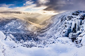 Winter paradise. Amazing sunrise in the mountains. Cold, freeze, wind yet very beautiful and relaxing view down to a valley on snow covered trees. Sun peaking through the clouds.