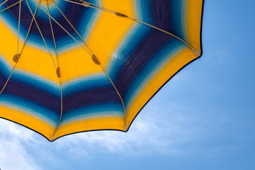 Bright yellow-blue beach umbrella with blue sky. Beach holiday.