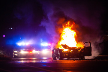 Car on fire at night with police lights in background