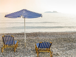 Liegestühle und Sonnenschirm an steinigem Strand auf Kreta, Griechenland