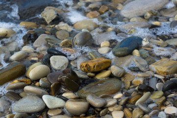 pebble stones on the sea beach, the rolling waves of the sea with foam