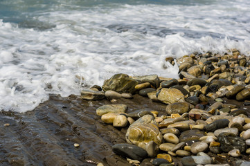 pebble stones on the sea beach, the rolling waves of the sea with foam