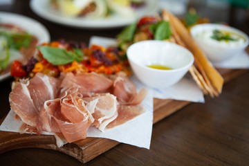 Delicious Prosciutto di Parma or Parma with colorful Bruschetta topped with grilled cherry tomatoes on a wooden board. Natural light.