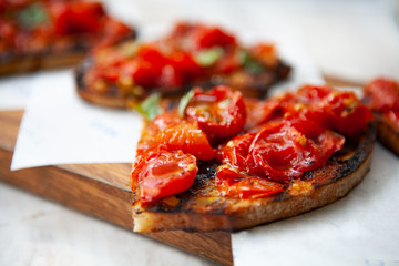 Delicious and colorful Bruschetta made with grilled cherry tomatoes on top of toasted bread rubbed with garlic, dressed with basil, olive oil and salt on a wooden board. Natural light.