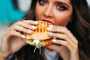 Close-up of unfocused girl with bright make up holding delicious crunchy cheeseburger in hands with...