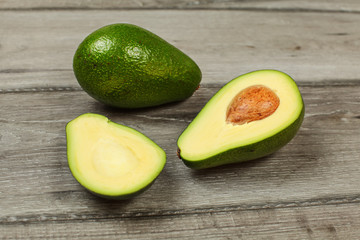 Avocado cut in half with whole pear in back, on gray wood table.