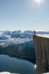 Young traveller hiker man standing on the Pulpit Rock, Preikestolen cliff edge and looking down the...