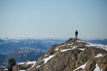 Rear view of hiker man standing on the Preikestolen rocks and looking at the beautiful mountains. Sunny winter day in Norway