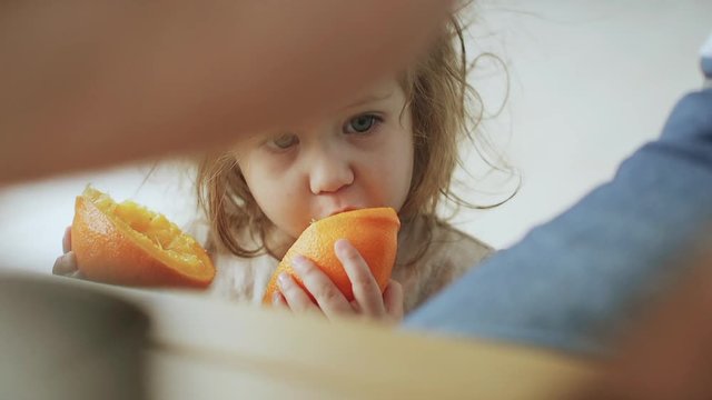 Cute little girl eating an orange, close up. Handheld