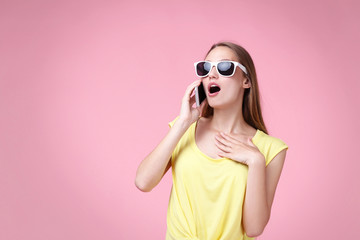 Portrait of young woman in sunglasses and smartphone on pink background