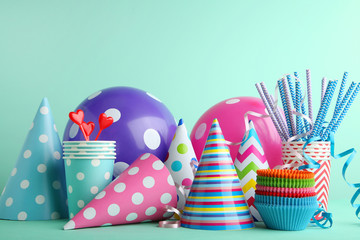 Birthday party caps, balloons and cups with paper straws on mint background
