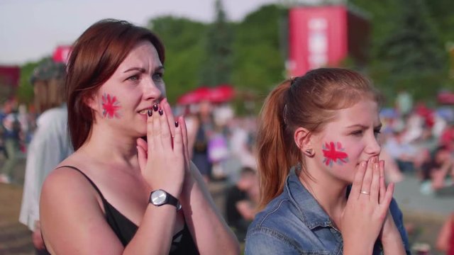 Girls with Britain flag on cheeks watch football match in fan zone