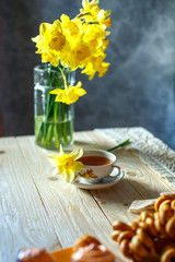 Fototapeta na wymiar a bouquet of yellow daffodils is in a vase and a Cup of tea on the table in the morning still life