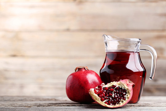 Pomegranate fruit and juice in jug on grey wooden table