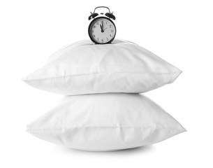 Soft pillows and alarm clock on white background