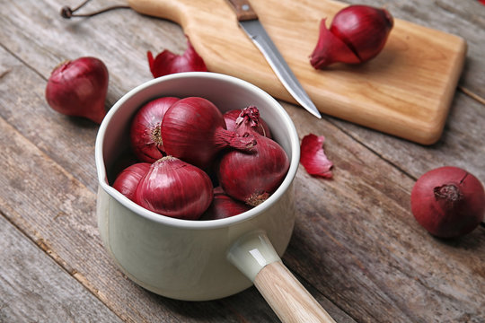 Saucepan with ripe red onions on wooden table