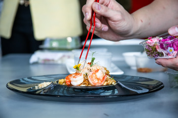 The chef prepares a dish of prawn noodles and decorates it with edible flowers.