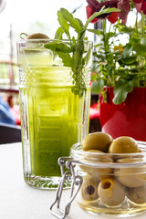 Lemonade from arugula in a glass and olives in a jar are on the table