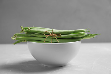 Bowl with tied fresh green beans on table