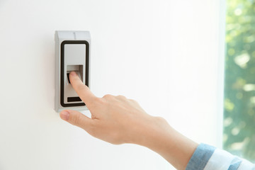 Young woman pressing fingerprint scanner on alarm system indoors