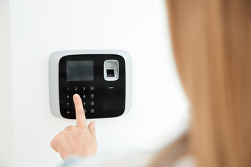 Young woman entering code on alarm system keypad indoors