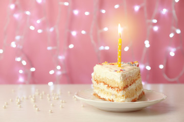 Slice of delicious birthday cake with candle on table