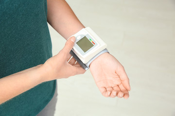 Young woman checking pulse with blood pressure monitor on wrist, closeup
